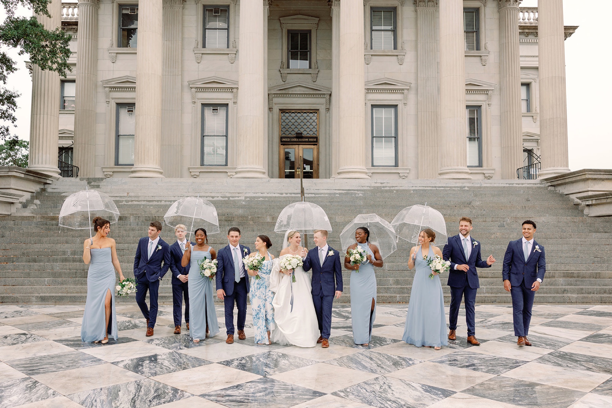 Bridal party walking down steps laughing with umbrellas
