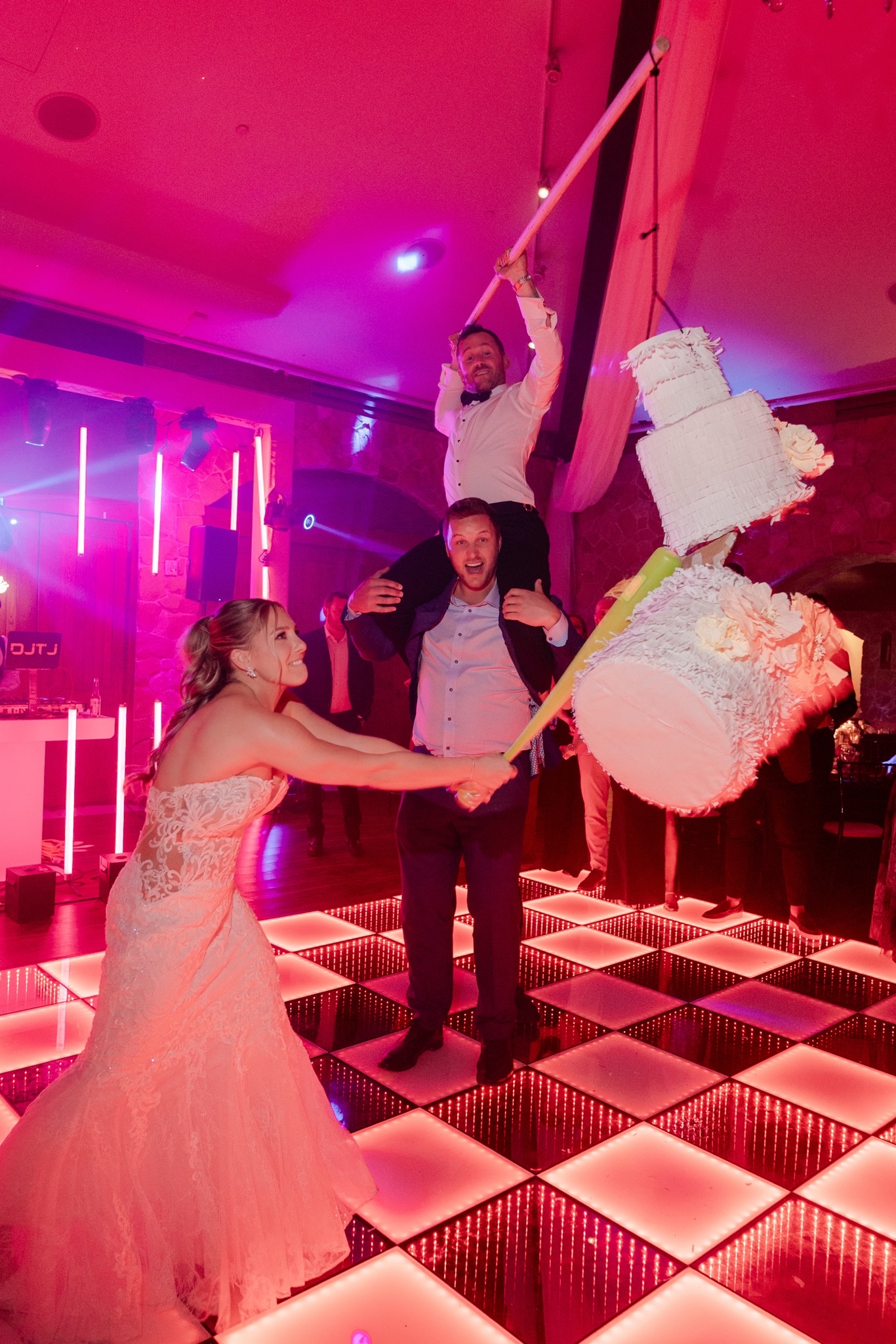 Bride breaking piñata while groom rides on guests' shoulders
