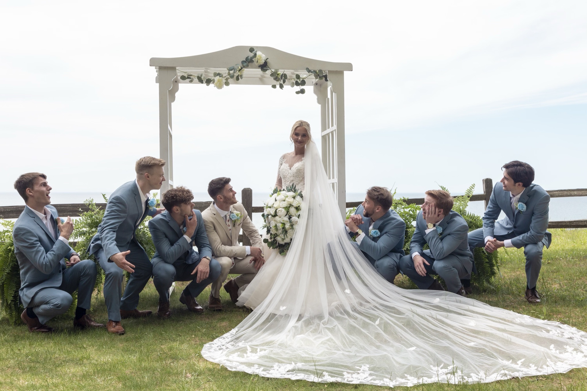 Bride standing while groomsmen kneel with big smiles